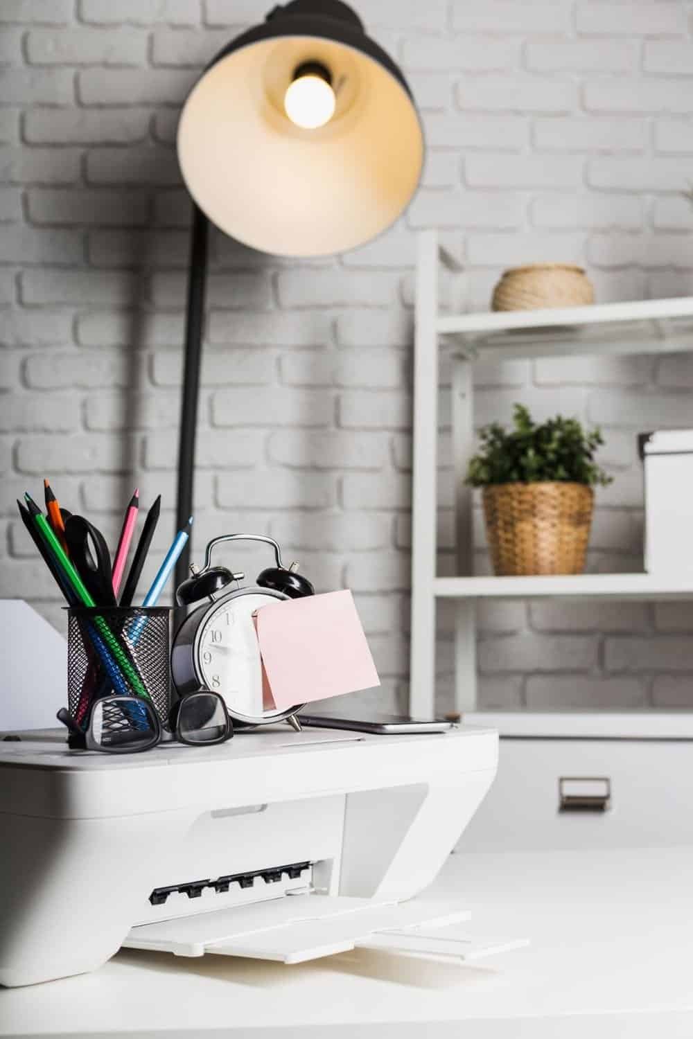 College Dorm Room Essentials-Desk setup with printer, stationery, and clock in a modern workspace highlighted by warm lamp light